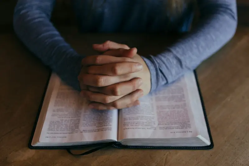Hands folded in prayer on an open Bible