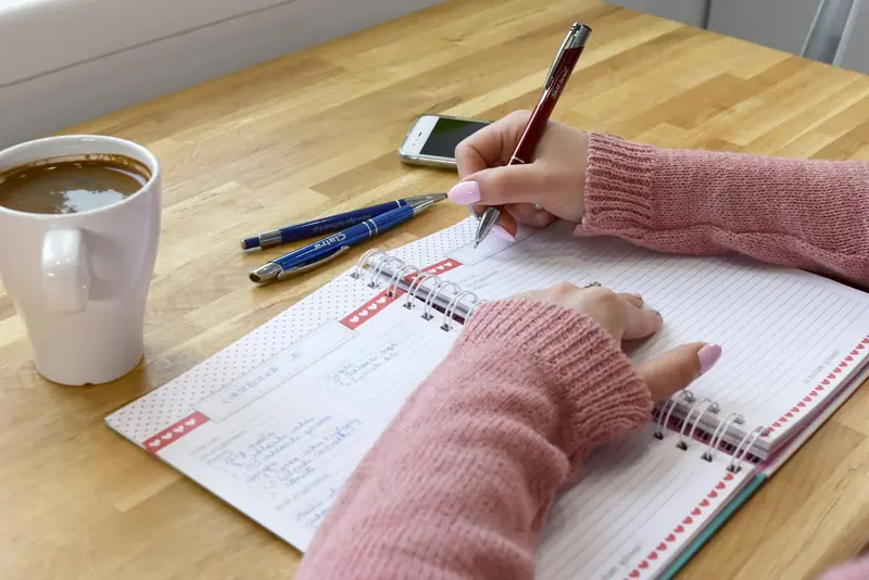Noen skriver i en notatbok ved siden av en kopp kaffe